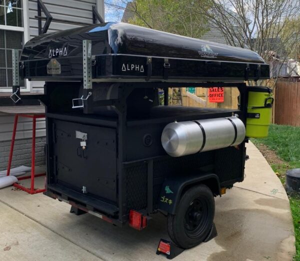 A black trailer with a large metal box on it's back.