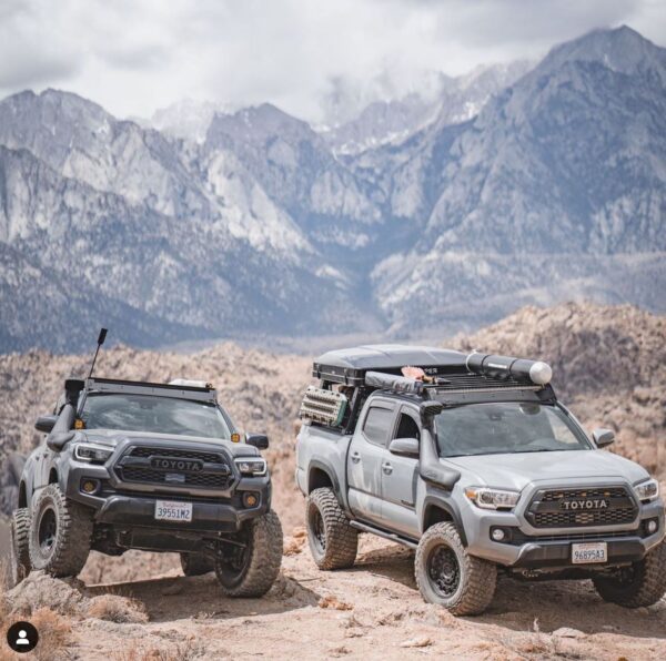 Two trucks parked in the desert with mountains behind them.